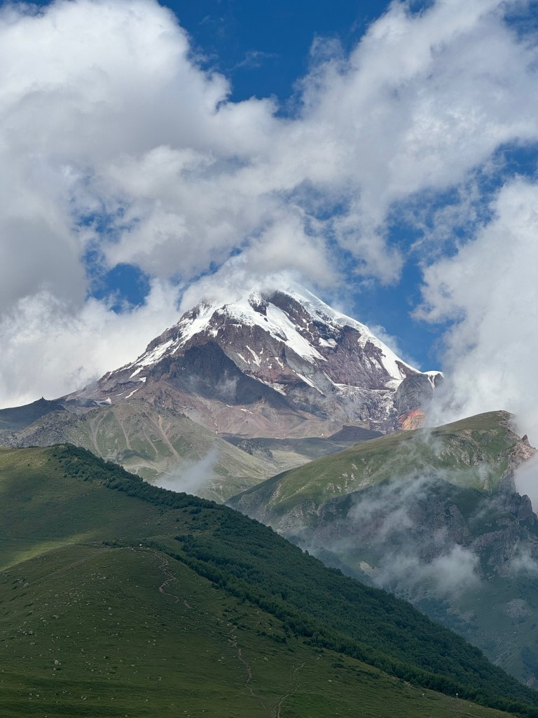 Snow-capped peak rising above green mountain ridges in the Georgian Caucasus - photography by Sakine Gulec
