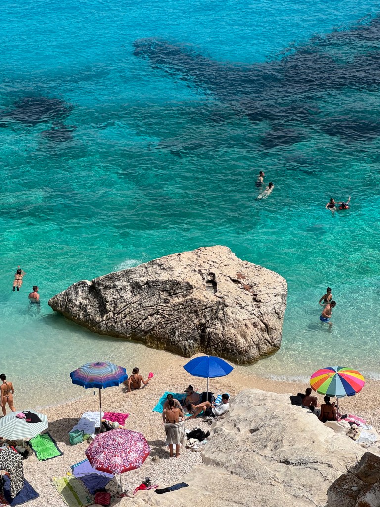 Turquoise cove with swimmers and beach umbrellas, Sardinia, Italy - travel photography by Sakine Gulec